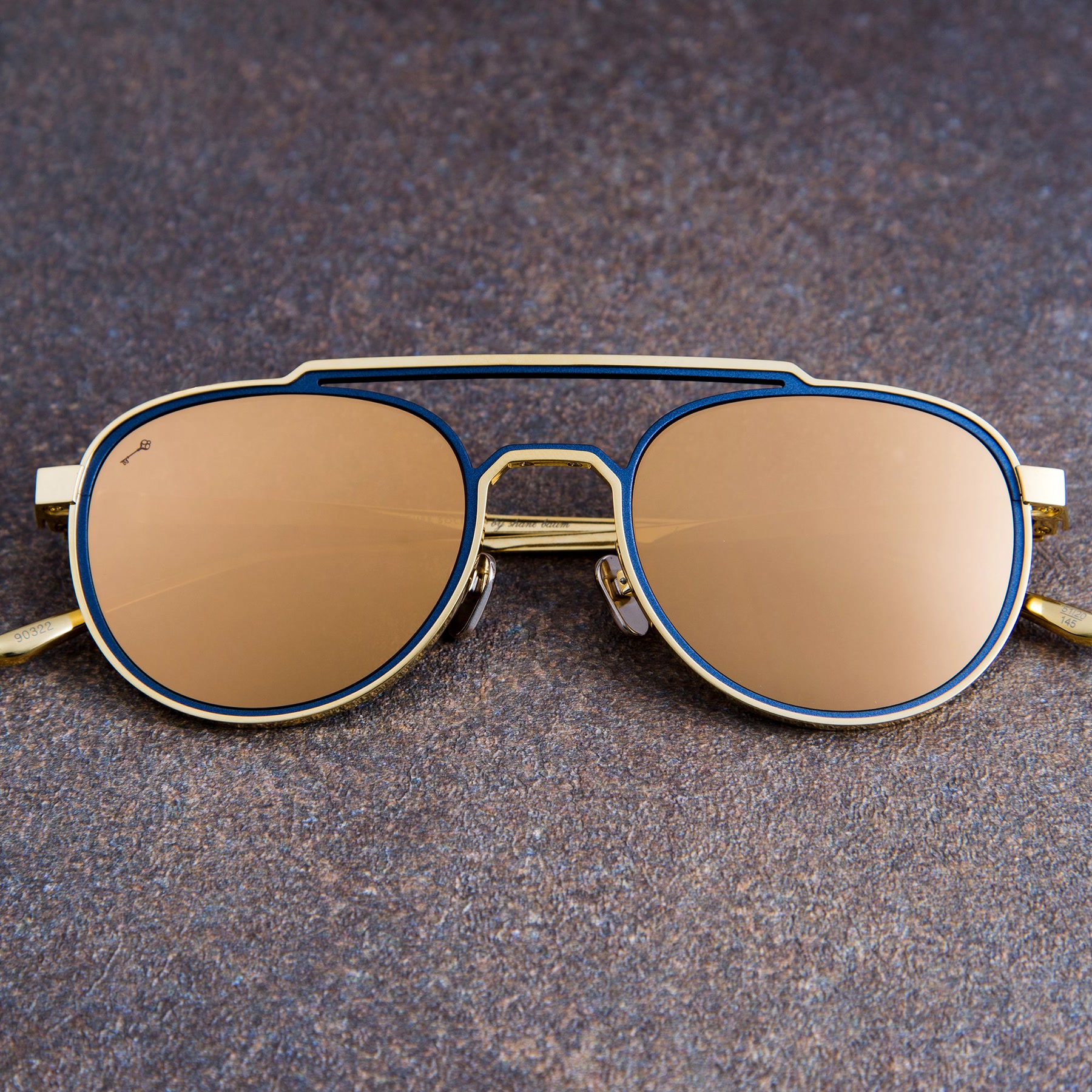 Clairaut frame with transition lenses in 24K gold and navy, front view on dark stone
