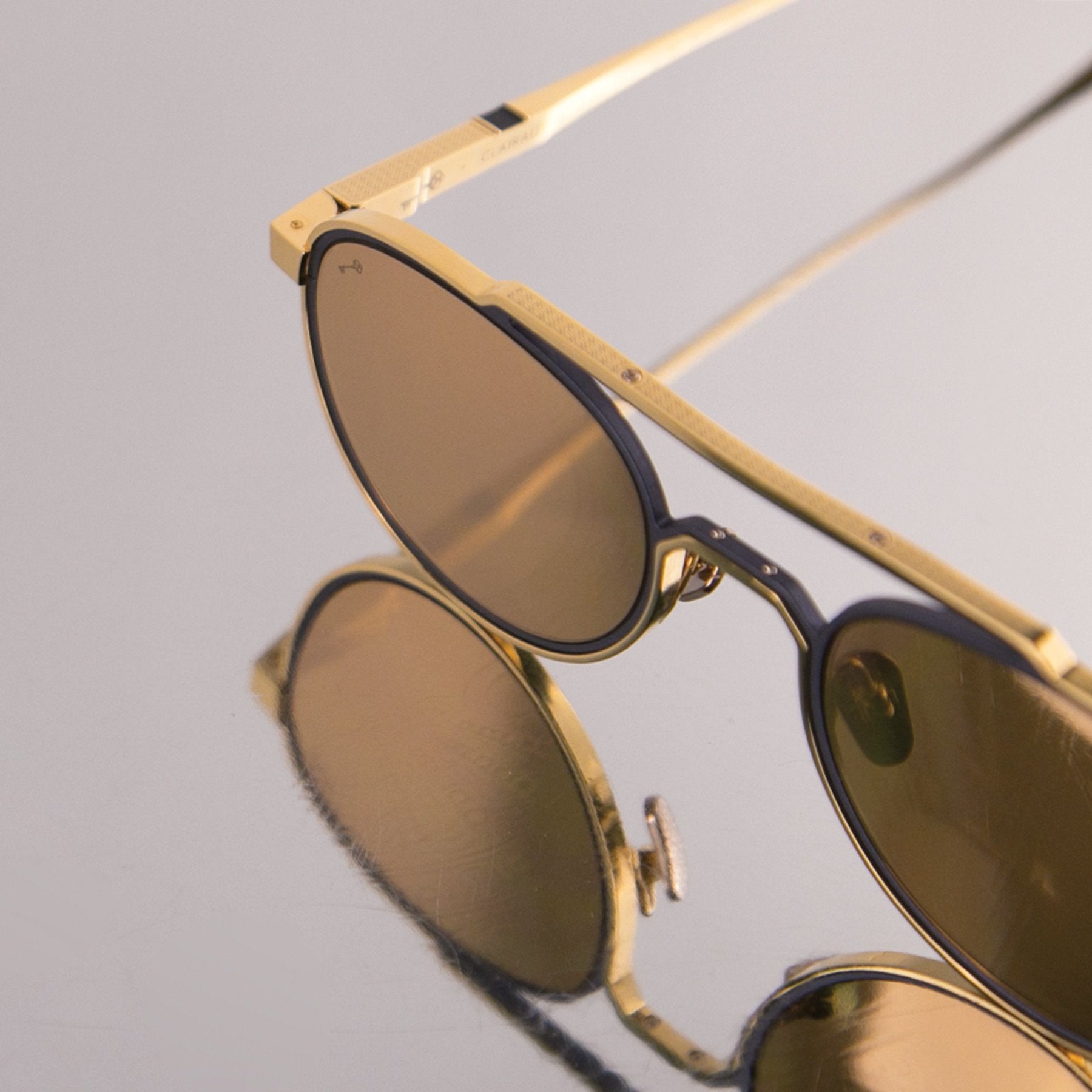 Clairaut frame with transition lenses in 24K gold and navy, reflected on a mirror